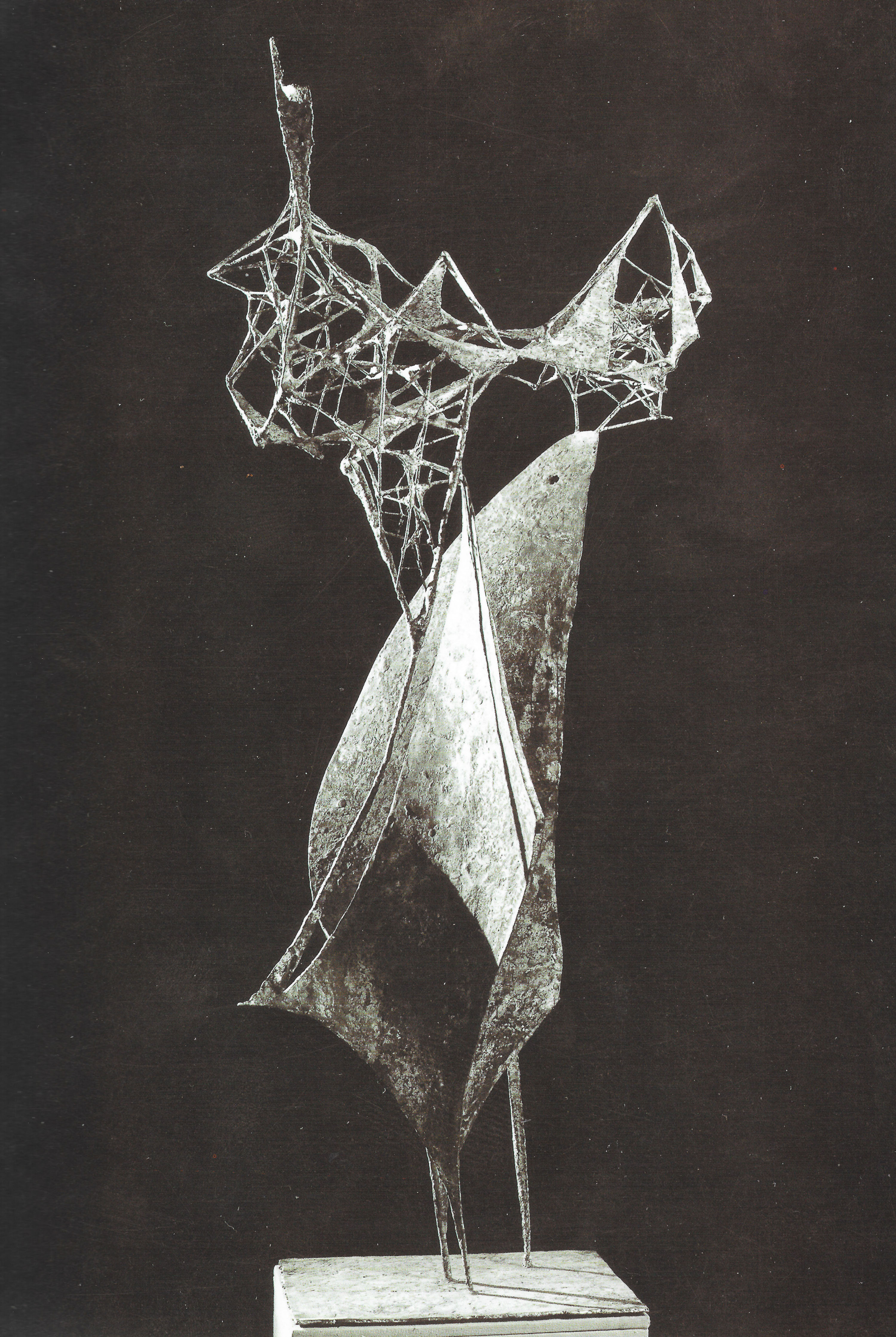 Sculpture. Black and white photograph of a bronze, abstract form. An elongated, triangular piece resting on three pointed legs is reminiscent of an animal or bird, a beak or muzzle stretched up. A cloud like a spider’s web whipped in wind rises above.